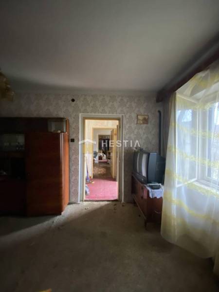 Ein Zimmer in einem Einfamilienhaus mit Retro-Möbeln, einem alten Fernseher, einem Fenster mit Blumen-Vorhängen.