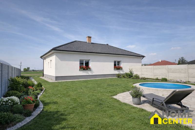 Ein Einfamilienhaus in Zemianska Olča mit Rasen, Pool und Blumenbepflanzung auf dem Grundstück.