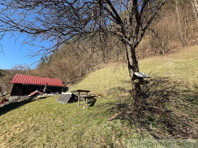 Eine Hütte bei Moštenica, umgeben von Bäumen und grasbewachsenen Hügeln bei sonnigem Wetter.