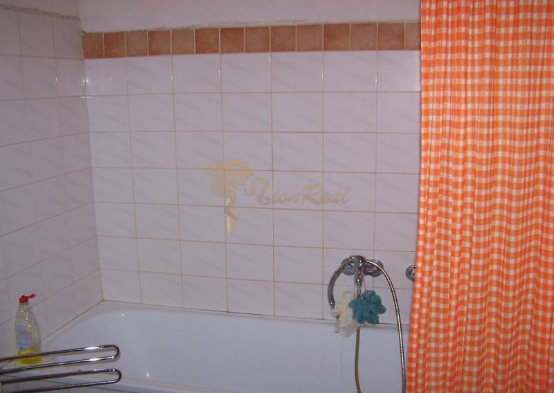Badezimmer mit Badewanne, orangem Vorhang und Fliesen in einer 2-Zimmer-Wohnung.