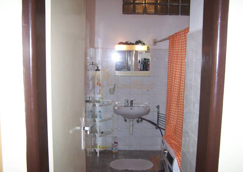 Badezimmer in einer 2-Zimmer-Wohnung mit weißem Waschbecken, Dusche und orangefarbenem Vorhang.