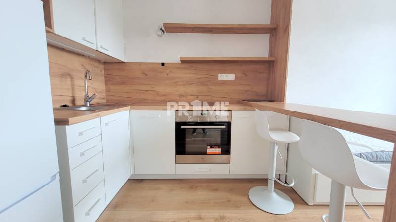 Eine Küche in einem Studio-Apartment mit weißen Schränken und einem Boden in Holzoptik.