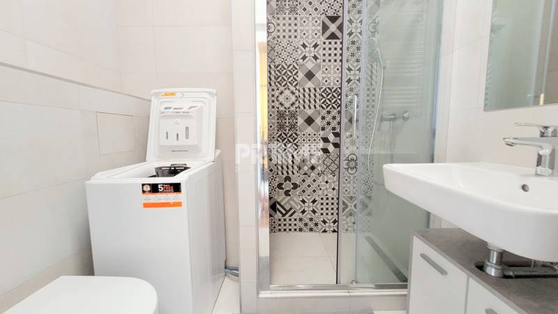 Badezimmer in einem Studio-Apartment mit Waschmaschine und Duschkabine, dekorative Fliesen.