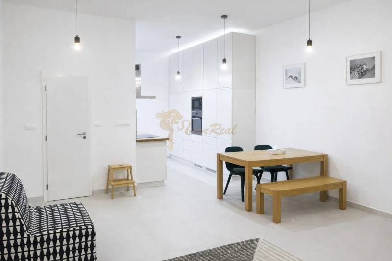 Innenraum einer 2-Zimmer-Wohnung mit weißen Wänden, einem Holztisch und einem schwarzen Sofa.