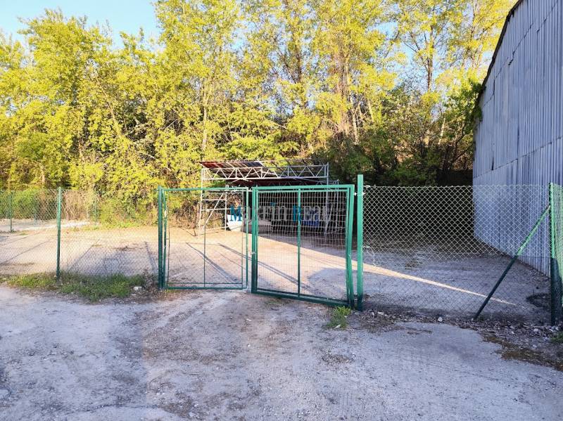 Ein Zaun mit einem Metallbauwerk, umgeben von Bäumen, im Gewerbegebiet von Nitra.