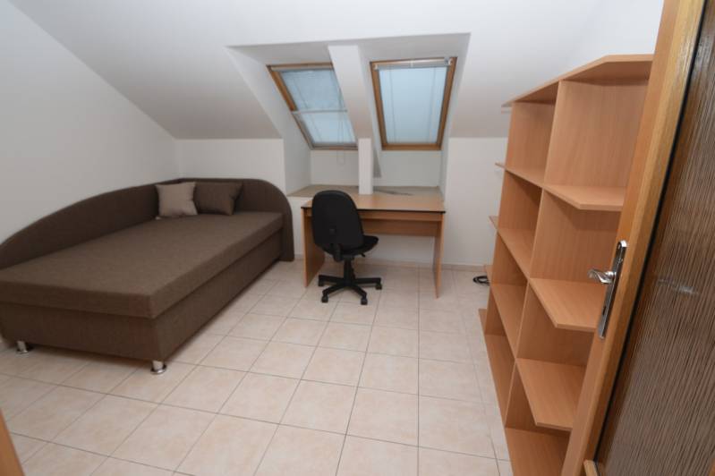 Ein Zimmer in einem Einfamilienhaus mit Bett, Tisch, Regalen, Fliesenboden und Dachfenstern.