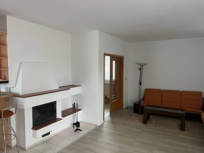 Wohnzimmer mit Kamin, orangefarbenem Sofa, Holzboden und Glastisch.