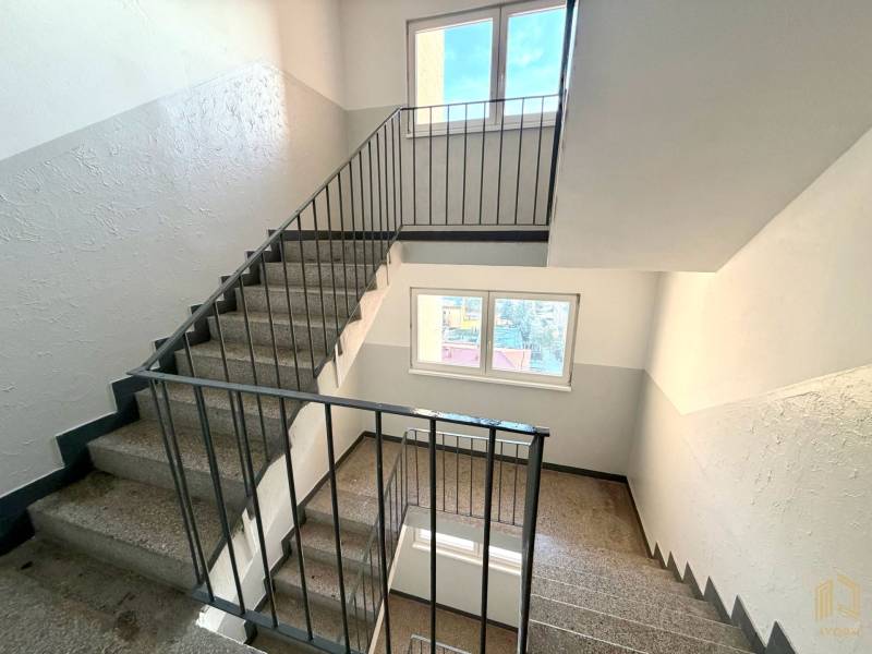 Eine Treppe in einem Studio-Apartment mit Fenstern, weißen Wänden und einem Metallgeländer.