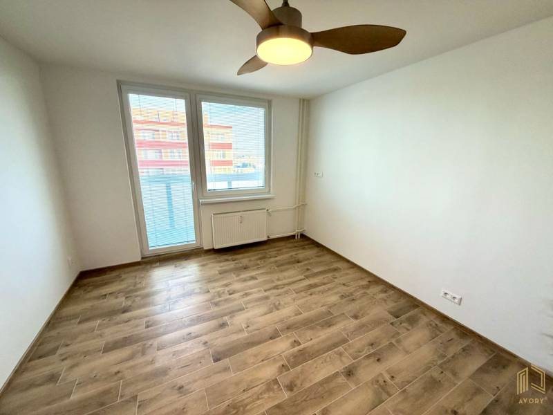 Ein Zimmer in einem Studio-Apartment mit einem Boden in Holzoptik, einem Deckenventilator und einem Fenster mit Aussicht.