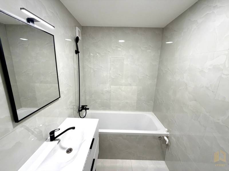 Badezimmer in einem Studio-Apartment mit Dusche, Badewanne, Waschbecken und Spiegel.