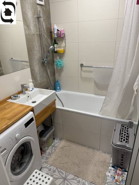 Badezimmer mit Duschwanne und Waschmaschine in einer 4-Zimmer-Wohnung mit eleganten Fliesen.