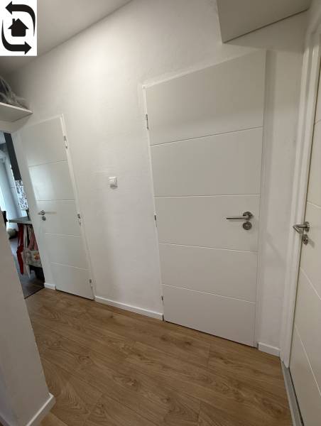 Der Flur in einer 4-Zimmer-Wohnung mit weißen Türen und einem Boden in Holzoptik.