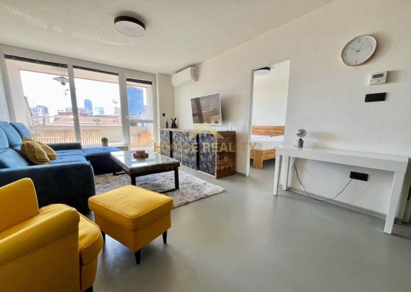 Wohnzimmer einer 3-Zimmer-Wohnung mit Sofa, Fernseher und Balkon.