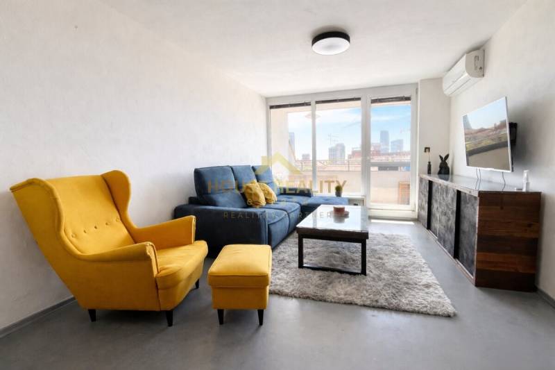 Wohnzimmer in einer 3-Zimmer-Wohnung mit gelbem Sessel, blauem Sofa und Fernseher an der Wand.