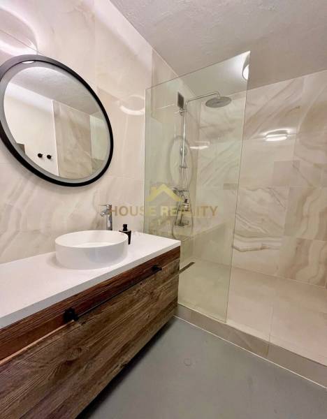 Badezimmer mit einem Holzschrank, einem runden Spiegel und einer Duschkabine in einer 3-Zimmer-Wohnung.