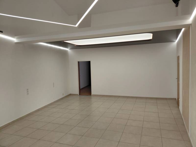 Gewerbeflächen mit weißen Wänden und Fliesenboden, Decke mit Streifenbeleuchtung.