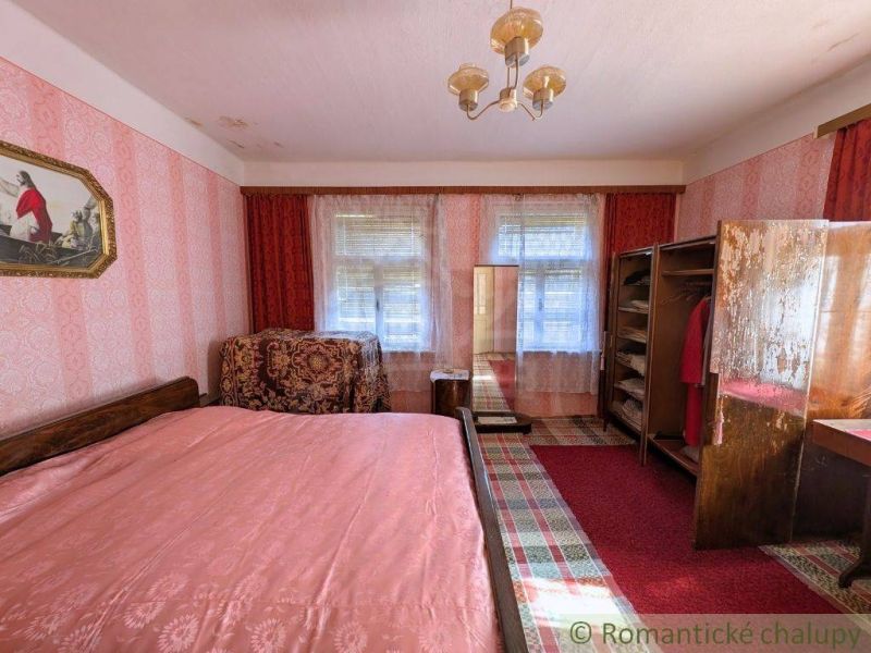 Schlafzimmer im Einfamilienhaus mit Bett, Kleiderschrank und rot-rosa Tapete.