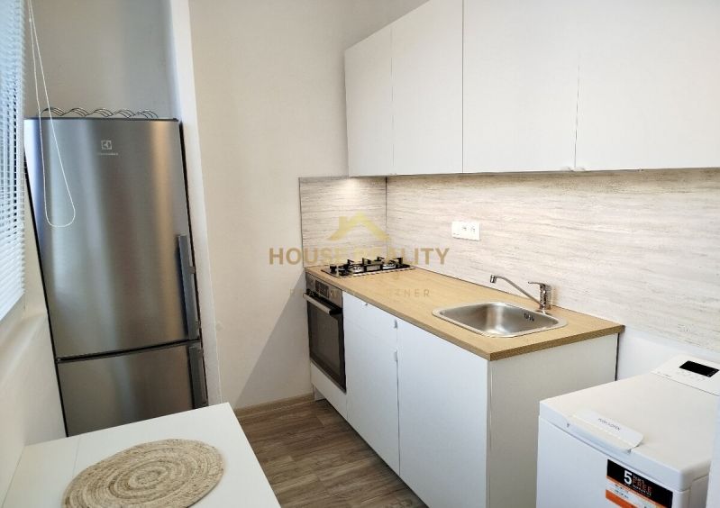 Küche in einer Einzimmerwohnung mit weißen Schränken, Kochfeld und Bodenbelag in Holzoptik.