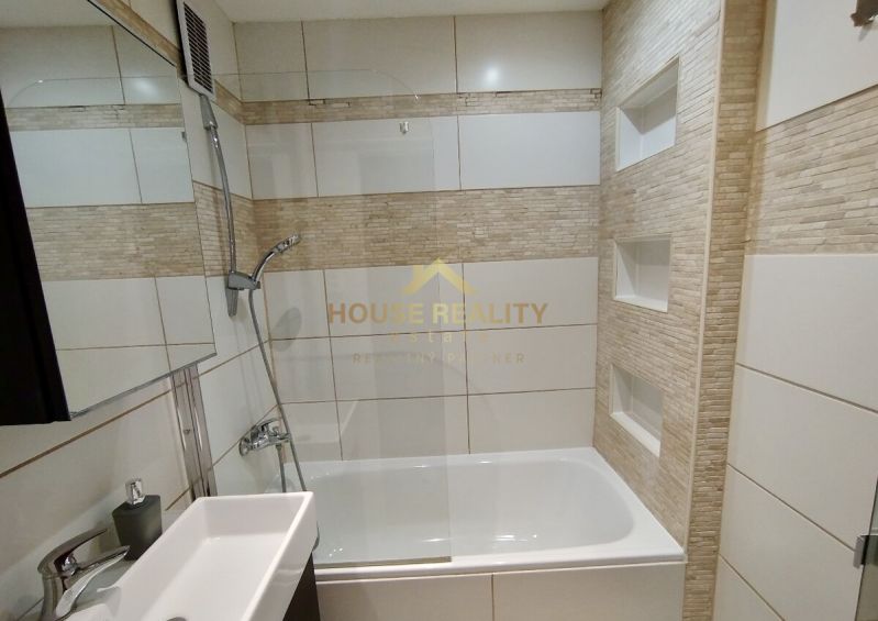 Badezimmer in einer Einzimmerwohnung mit Badewanne und Duschkopf, gefliest.