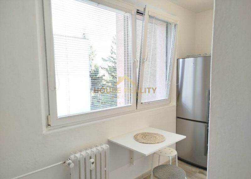 Küchenecke in einer Einzimmerwohnung mit Fenster, kleinem Tisch und Kühlschrank.