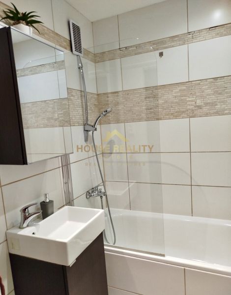 Badezimmer in einer Einzimmerwohnung mit Badewanne, Waschbecken und Fliesen in Beigetönen.