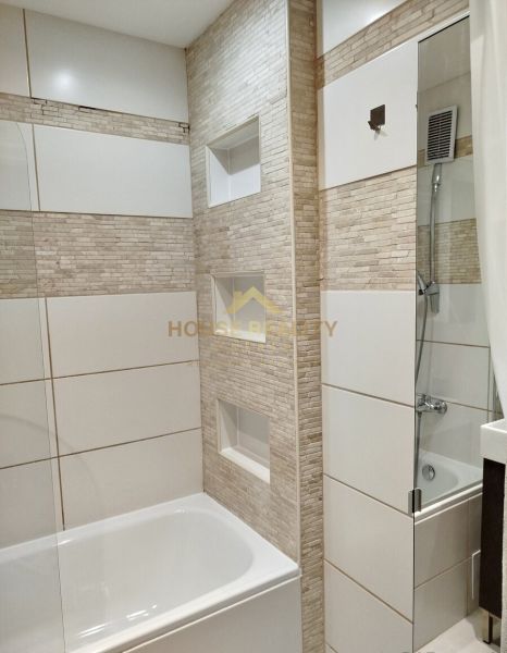 Badezimmer in einer Einzimmerwohnung mit Badewanne und Fliesen in Beigetönen.