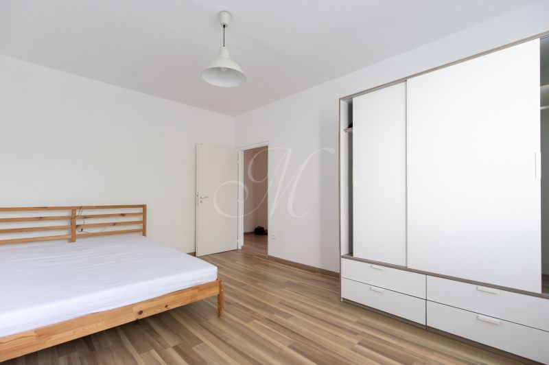 Schlafzimmer mit einem Holzbett, einem weißen Schrank und einem Boden mit Holzdekor in einer 3-Zimmer-Wohnung.