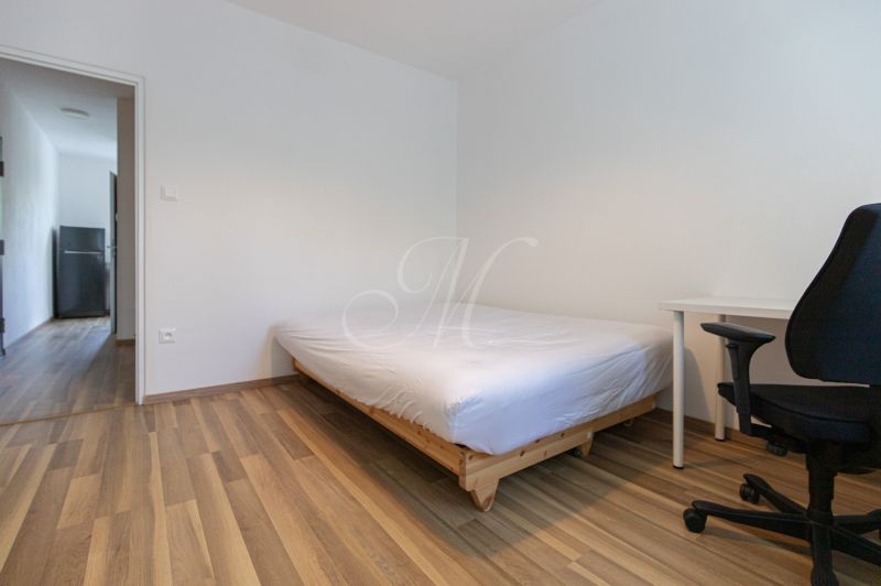 Ein Schlafzimmer in einer 3-Zimmer-Wohnung mit einem Bett, einem Schreibtisch und einem Boden in Holzoptik.