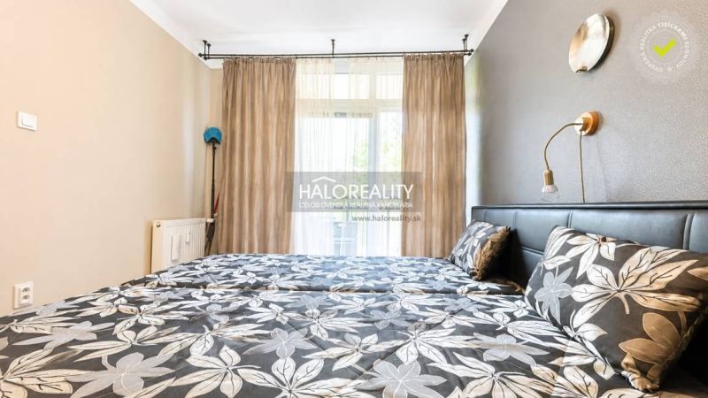 Schlafzimmer in einer 3-Zimmer-Wohnung mit Blumenmuster auf der Bettwäsche und Vorhängen.