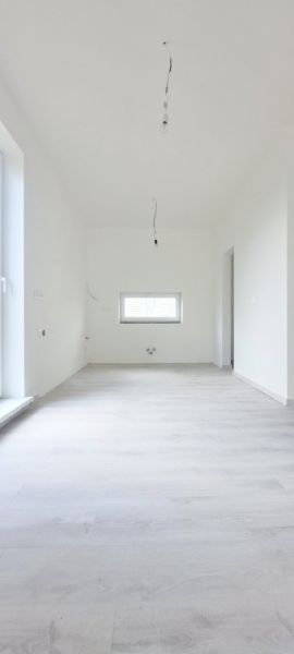 Ein Zimmer in einem Einfamilienhaus mit weißen Wänden und einem Boden in Holzoptik.