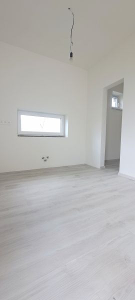Ein Zimmer in einem Einfamilienhaus mit einem Holzboden und einem kleinen Fenster.