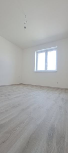 Ein Zimmer mit einem Fenster und einem Boden in Holzoptik in einem Einfamilienhaus.