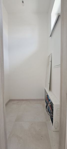 Úzka miestnosť s rozvádzačom v rodinnom dome, svetlé dlaždice, neutrálne steny.