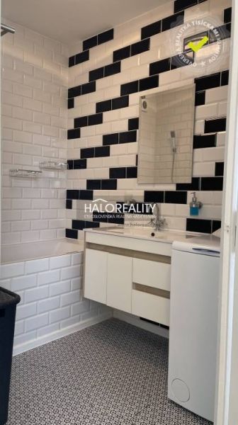 Badezimmer in einer 2-Zimmer-Wohnung mit Mosaikboden, schwarz-weißen Fliesen und Waschbecken.