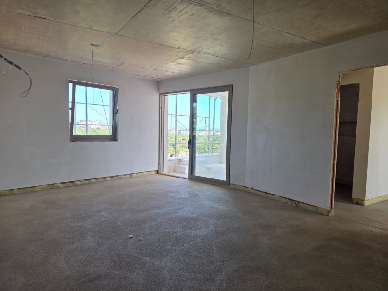 Ein Zimmer in einer 3-Zimmer-Wohnung mit einem rohen Betonboden und weißen Wänden.