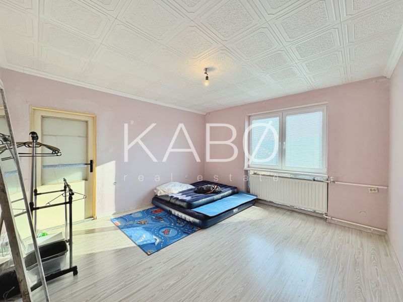 Ein Zimmer in einem Einfamilienhaus mit einer Matratze auf dem Boden, hellrosa Wände und ein großes Fenster.