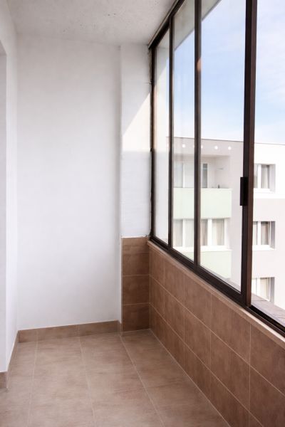 Ein verglaster Balkon in einer 4-Zimmer-Wohnung mit hellem Fliesenboden und Blick auf ein Wohngebäude.