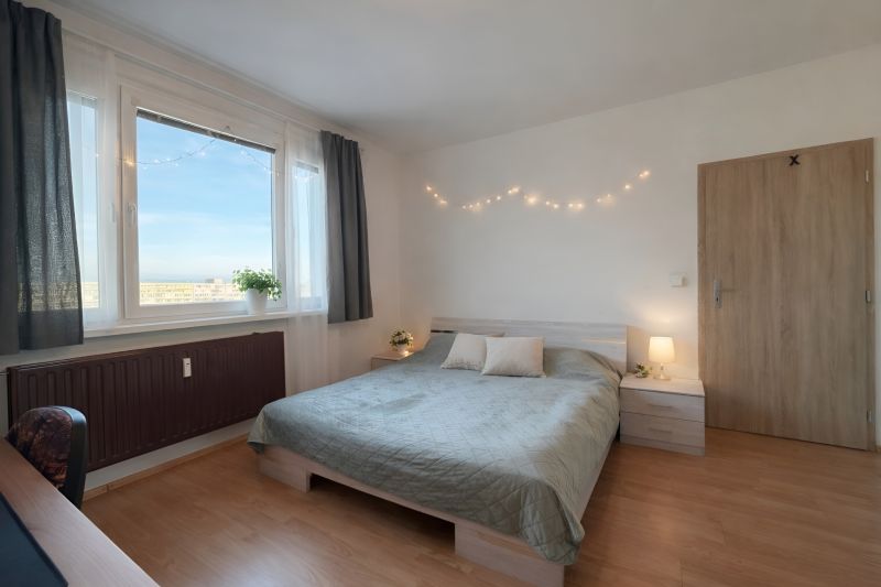 Schlafzimmer in einer 4-Zimmer-Wohnung mit Bett, Vorhängen und Boden in Holzoptik.