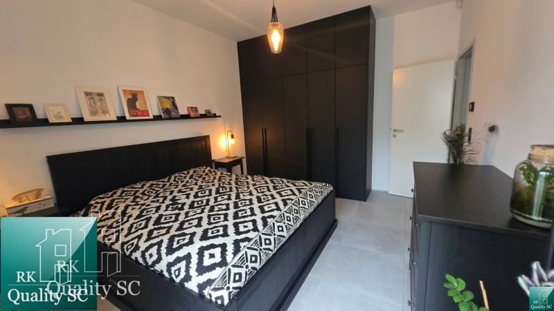 Schlafzimmer mit schwarzen Möbeln, künstlerischen Dekorationen und gemustertem Bettüberwurf.