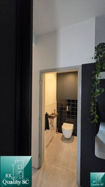 Toilette im Einfamilienhaus mit schwarzen Fliesen und hellem Boden.