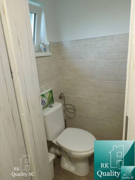 Toilette in einer Hütte mit Holzboden und beigefarbenen Fliesen.
