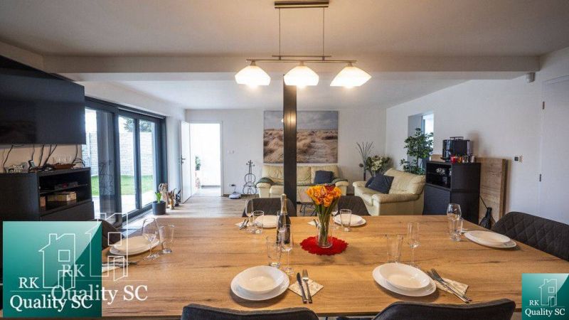 Esstisch mit Gläsern und Tellern in einem Einfamilienhaus, im Hintergrund das Wohnzimmer.