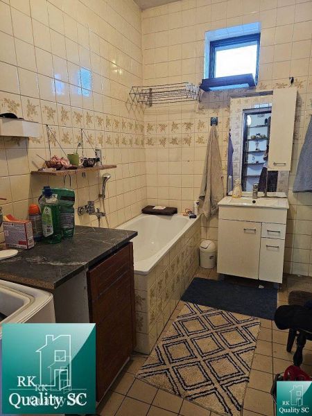 Badezimmer in einem Einfamilienhaus mit Badewanne, Waschbecken und Aufbewahrungsschränken. Geflieste Wände.