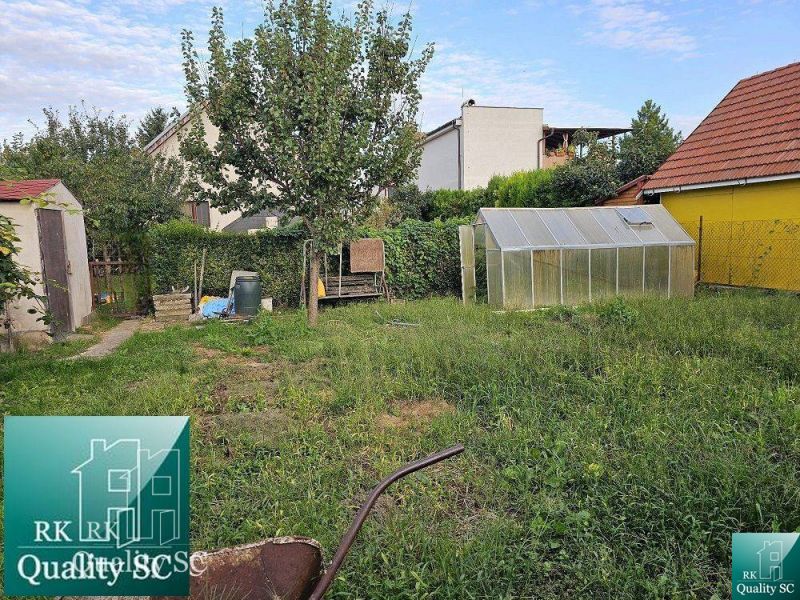 Der Garten des Einfamilienhauses in Turany mit Rasen, Baum, Gewächshaus und Nebengebäude.