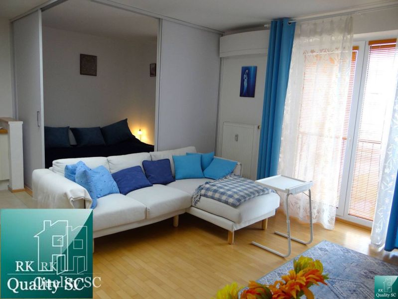 Innenraum einer Einzimmerwohnung mit Holzboden, weißem Sofa und blauen Accessoires.