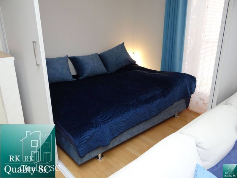 Blaues Bett mit Kissen in einer Einzimmerwohnung, Boden mit Holzdekor.