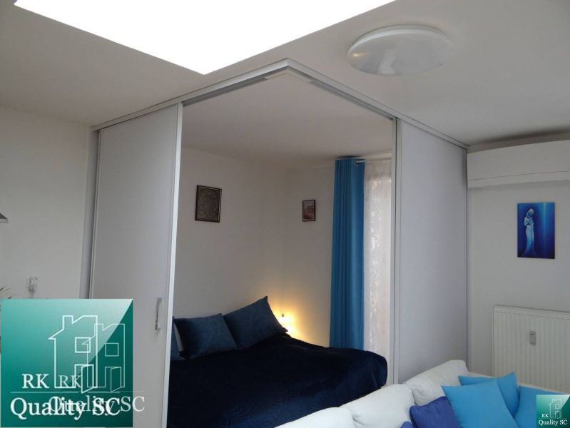 Schlafzimmer in einer Einzimmerwohnung mit blauen Vorhängen und Bildern an der Wand.