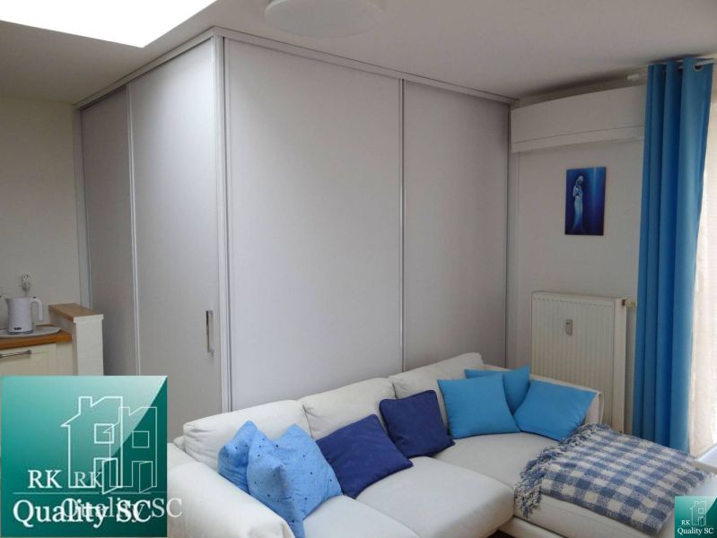 Helles Wohnzimmer in einer Einzimmerwohnung mit weißem Sofa und blauen Kissen.