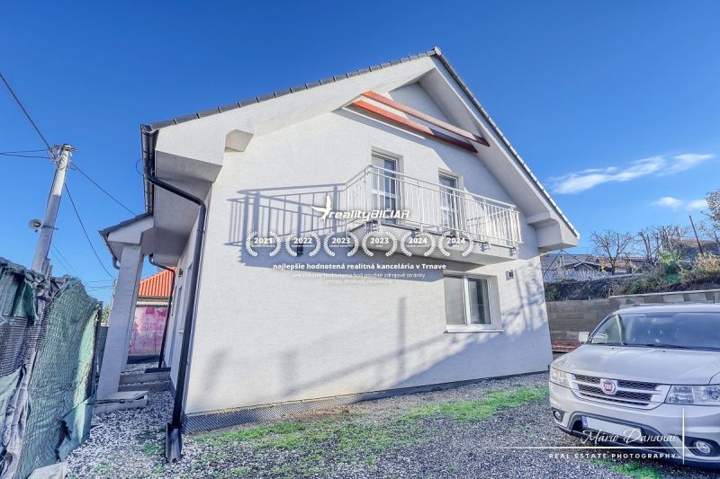 Ein Einfamilienhaus in Hrnčiarovce nad Parnou mit weißer Fassade und einem Balkon auf einem Kieshof.