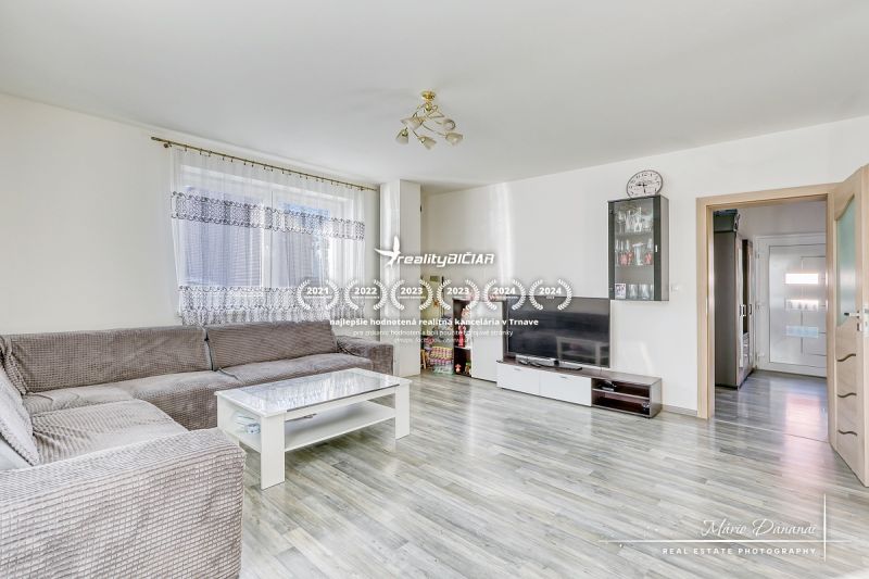 Wohnzimmer in einem Einfamilienhaus mit einer Eckcouch und einem Boden in Holzoptik.